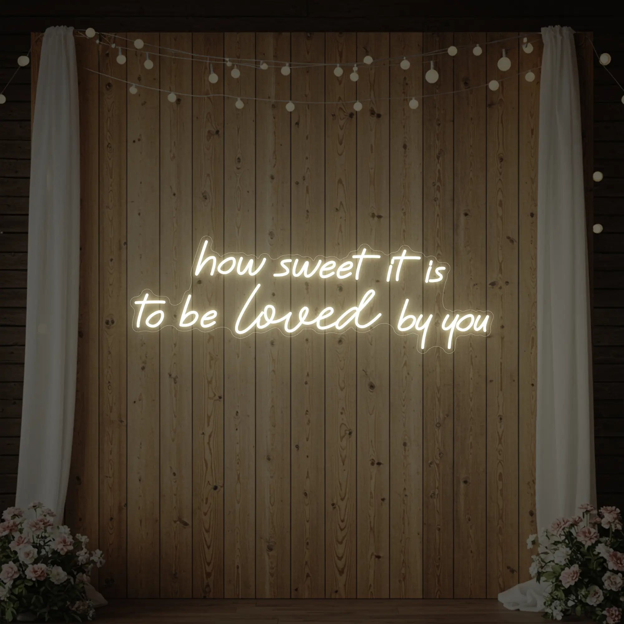 Photo of the 'How Sweet It Is To Be Loved By You' neon sign glowing in warm white against a styled interior wall.