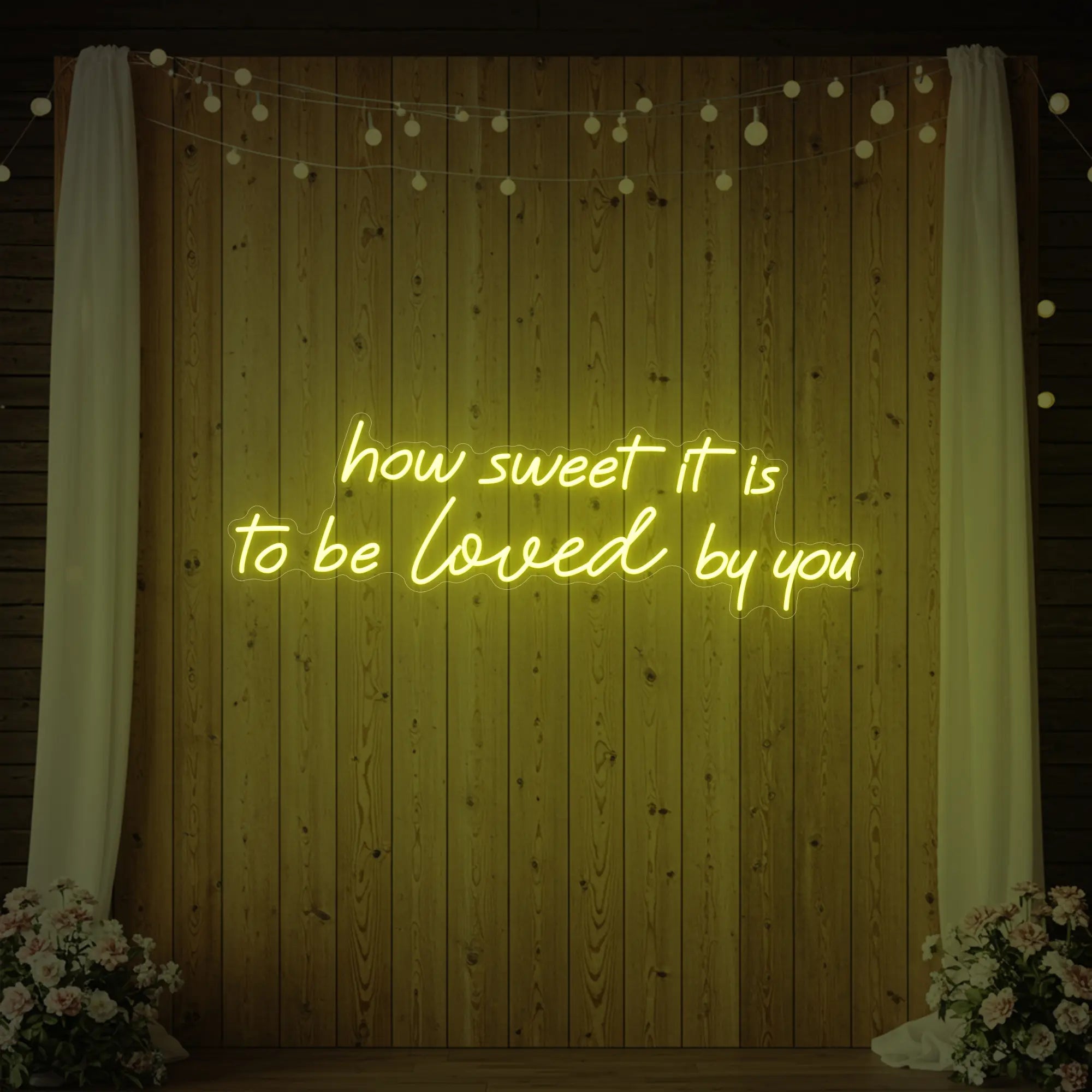 Photo of the 'How Sweet It Is To Be Loved By You' neon sign glowing in lemon yellow against a styled interior wall.