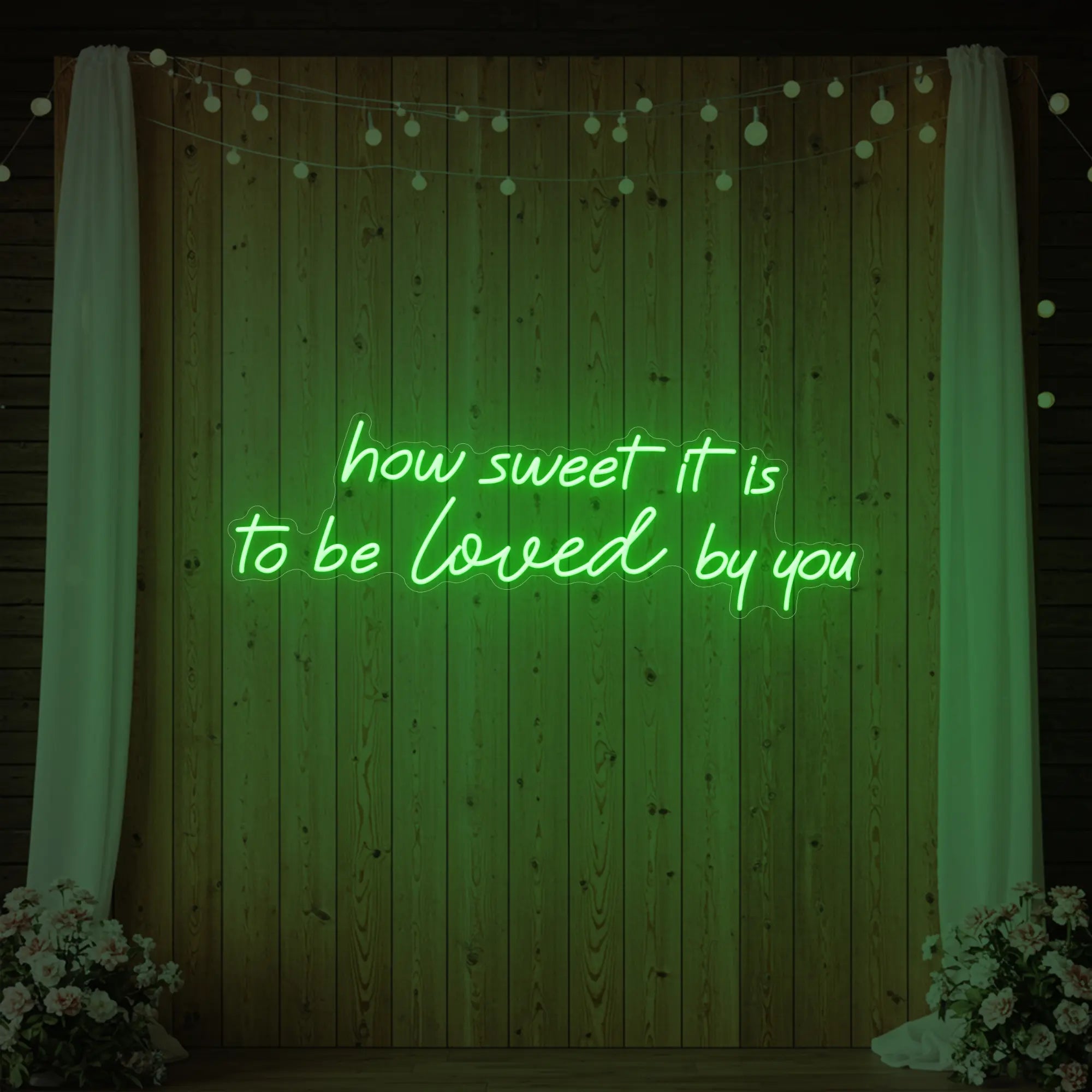 Photo of the 'How Sweet It Is To Be Loved By You' neon sign glowing in green against a styled interior wall.