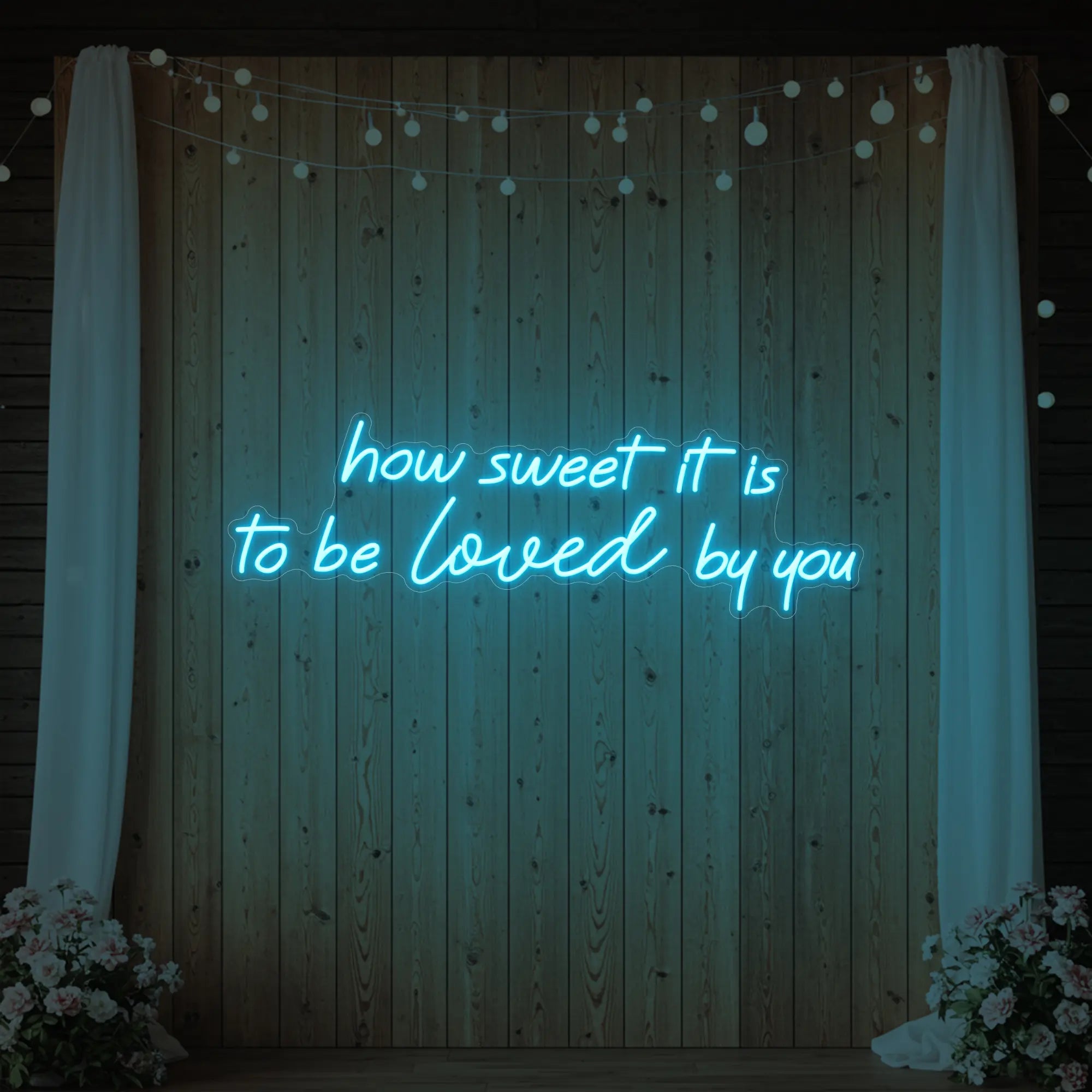 Photo of the 'How Sweet It Is To Be Loved By You' neon sign glowing in ice blue against a styled interior wall.
