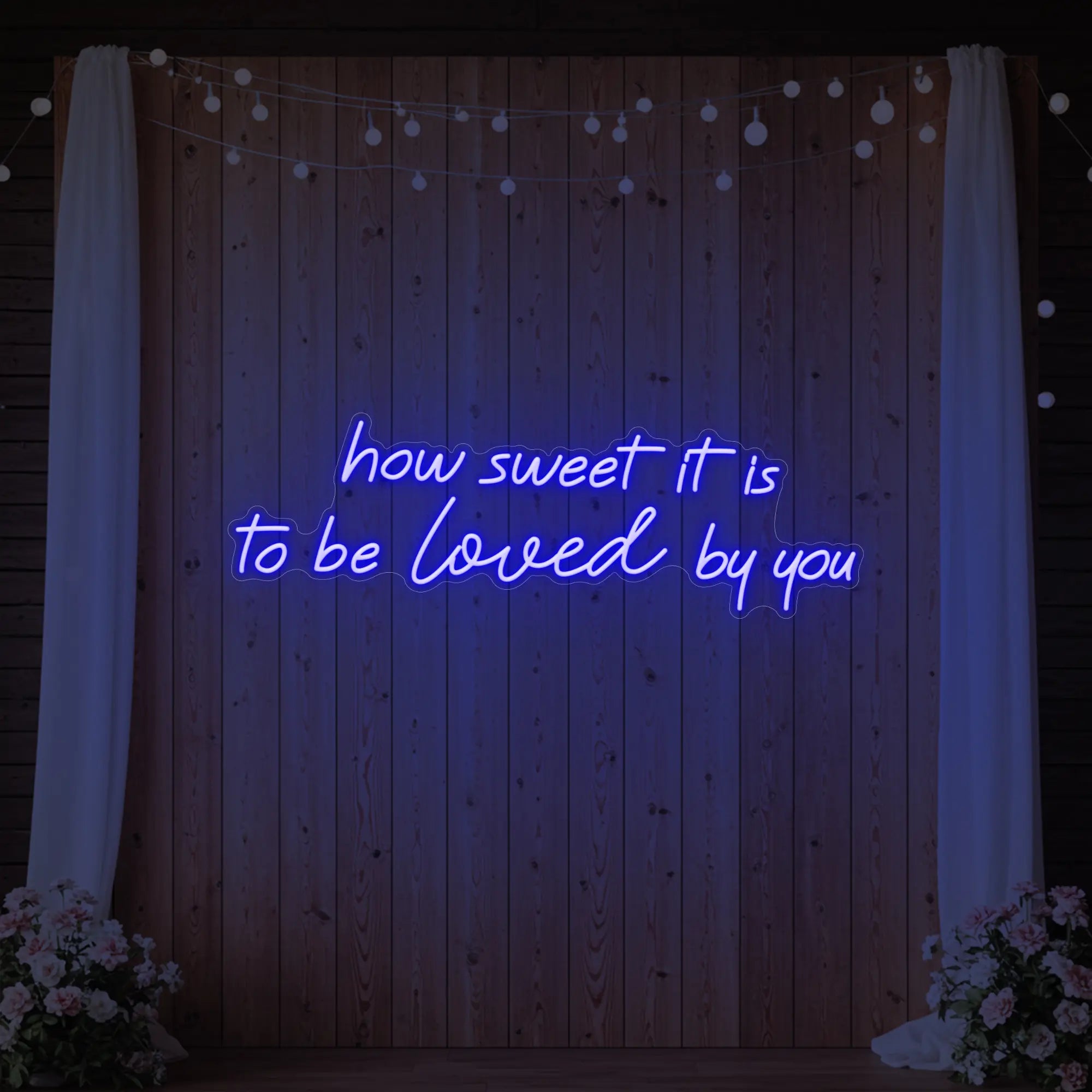 Photo of the 'How Sweet It Is To Be Loved By You' neon sign glowing in deep blue against a styled interior wall.