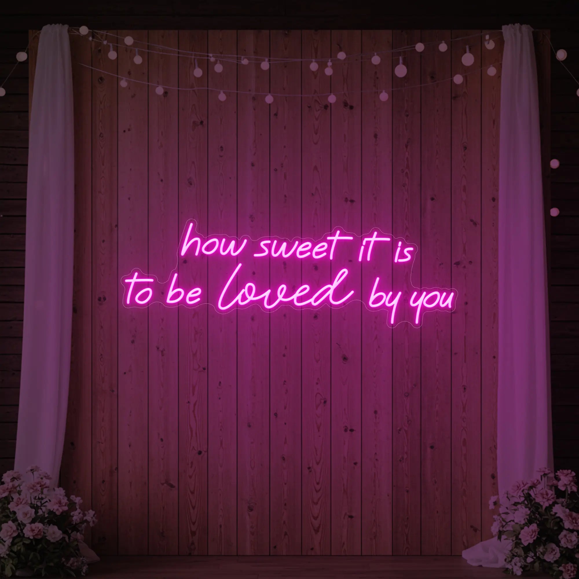 Photo of the 'How Sweet It Is To Be Loved By You' neon sign glowing in light pink against a styled interior wall.