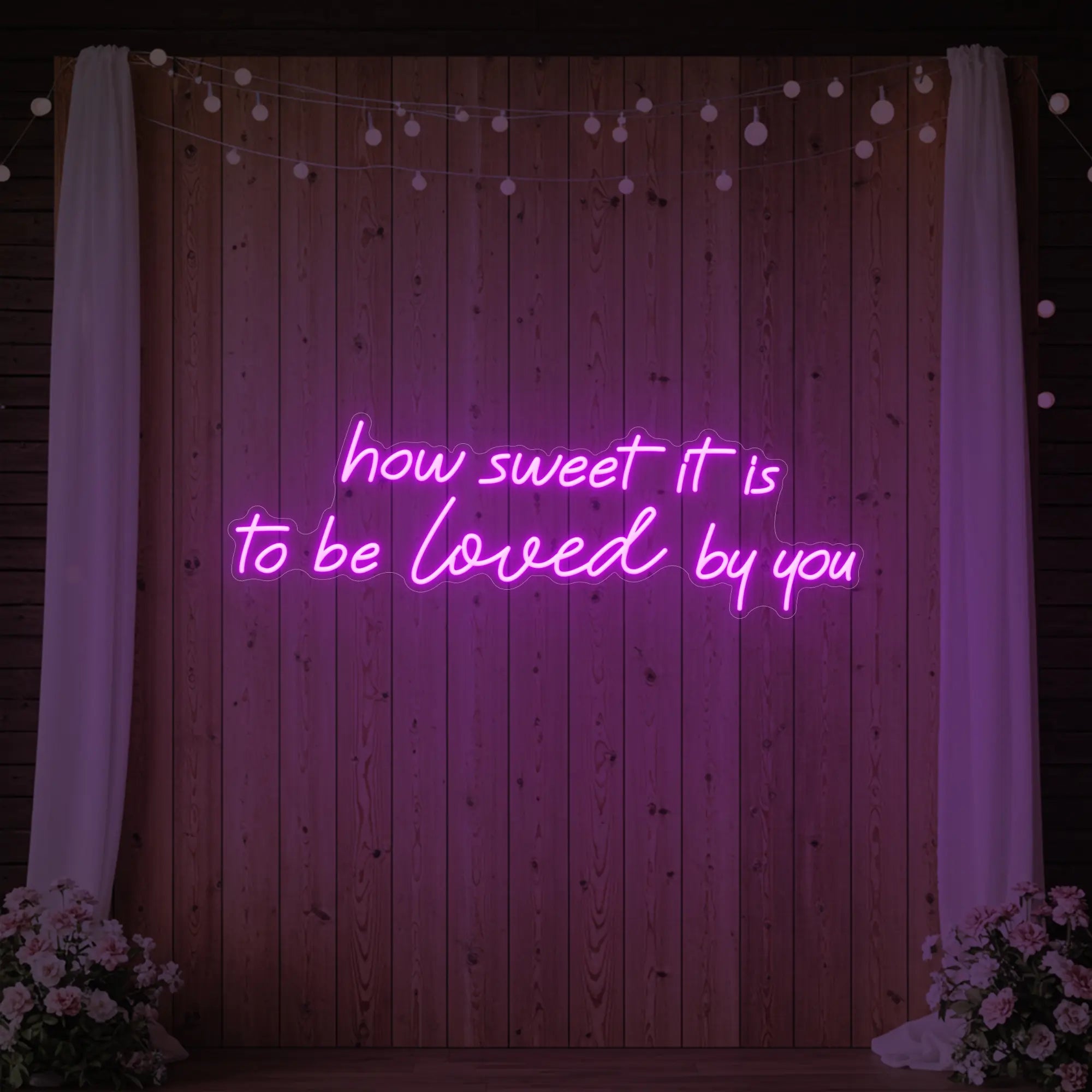 Photo of the 'How Sweet It Is To Be Loved By You' neon sign glowing in deep pink against a styled interior wall.