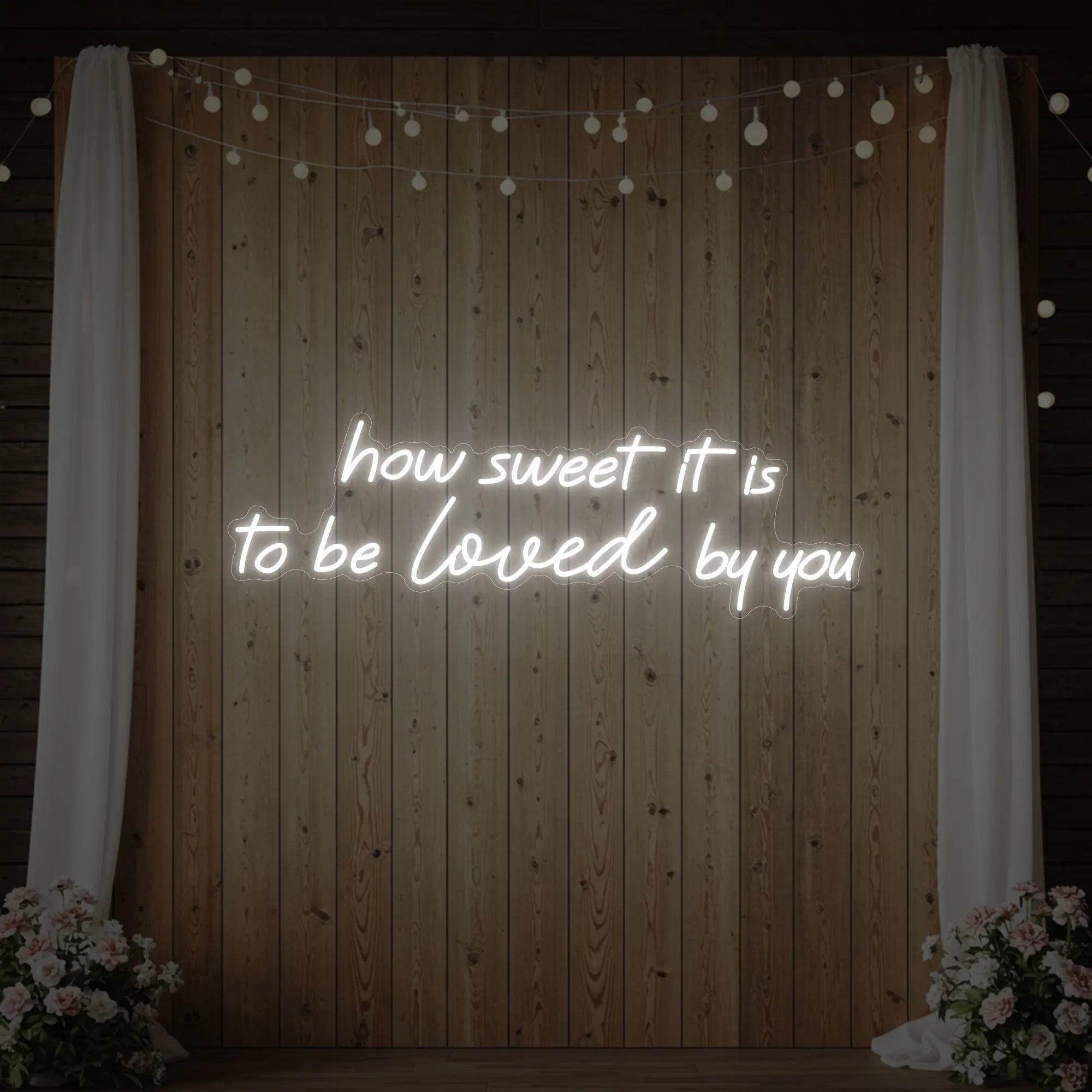 Photo of the 'How Sweet It Is To Be Loved By You' neon sign glowing in cool white against a styled interior wall.