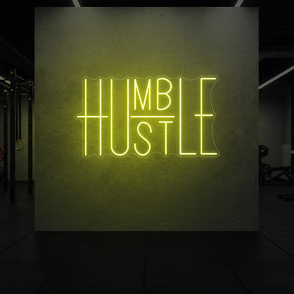 'Humble Hustle' neon sign glowing in lemon yellow against a styled interior wall.