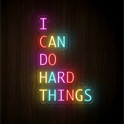“I CAN DO HARD THINGS” LED Neon Sign with multicolor pink, red, yellow, and cyan lettering on clear acrylic backing against a dark wood background, suited to home offices, study areas, and fitness spaces.