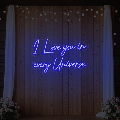 Photo of the 'I Love You In Every Universe' neon sign glowing in deep blue against a styled interior wall.