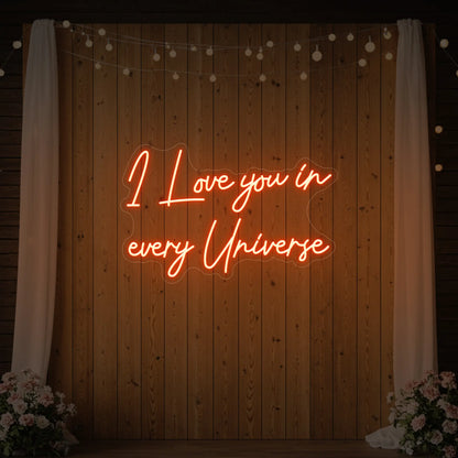 Photo of the 'I Love You In Every Universe' neon sign glowing in golden yellow against a styled interior wall.