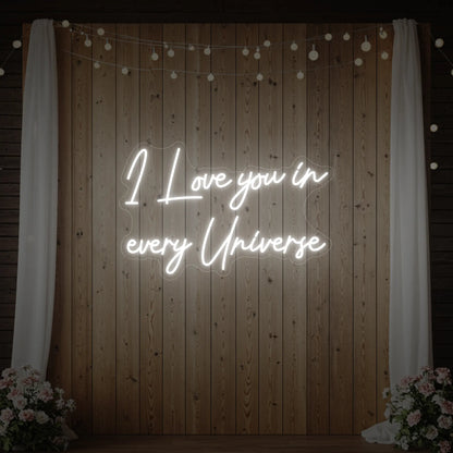 Photo of the 'I Love You In Every Universe' neon sign glowing in cool white against a styled interior wall.