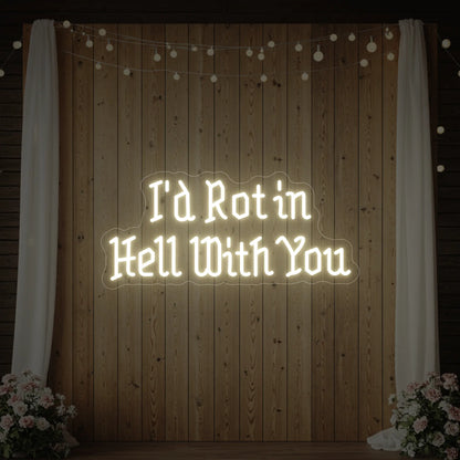 Photo of the 'I’d Rot in Hell With You' neon sign glowing in warm white against a styled interior wall.