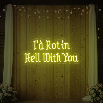 Photo of the 'I’d Rot in Hell With You' neon sign glowing in lemon yellow against a styled interior wall.