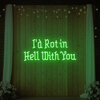 Photo of the 'I’d Rot in Hell With You' neon sign glowing in green against a styled interior wall.