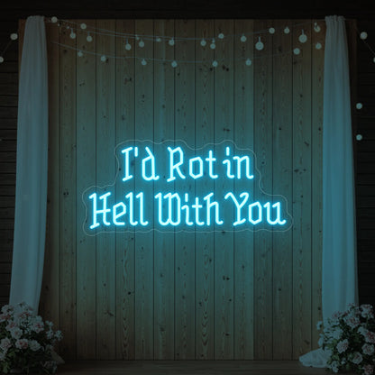 Photo of the 'I’d Rot in Hell With You' neon sign glowing in ice blue against a styled interior wall.