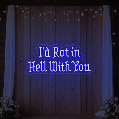 Photo of the 'I’d Rot in Hell With You' neon sign glowing in deep blue against a styled interior wall.