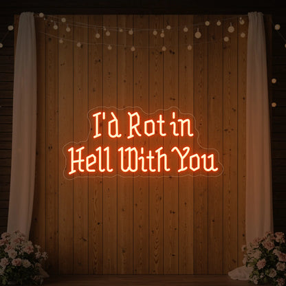 Photo of the 'I’d Rot in Hell With You' neon sign glowing in golden yellow against a styled interior wall.