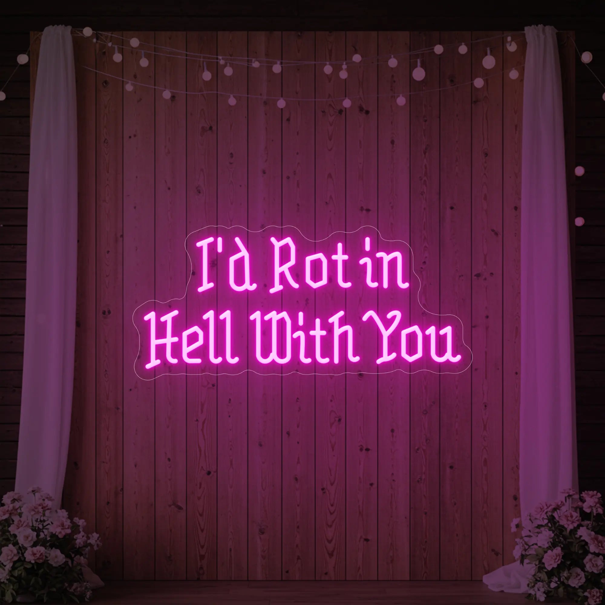 Photo of the 'I’d Rot in Hell With You' neon sign glowing in light pink against a styled interior wall.