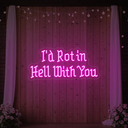 Photo of the 'I’d Rot in Hell With You' neon sign glowing in light pink against a styled interior wall.