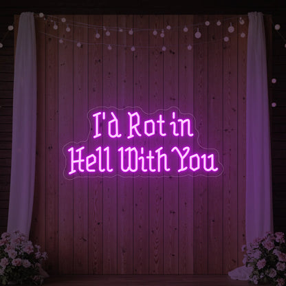 Photo of the 'I’d Rot in Hell With You' neon sign glowing in deep pink against a styled interior wall.