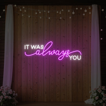 Photo of the 'It Was Always You' neon sign glowing in deep pink against a styled interior wall.