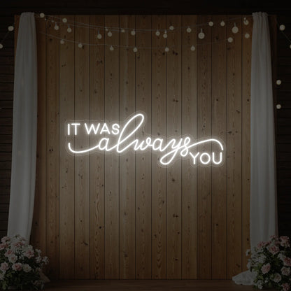Photo of the 'It Was Always You' neon sign glowing in cool white against a styled interior wall.