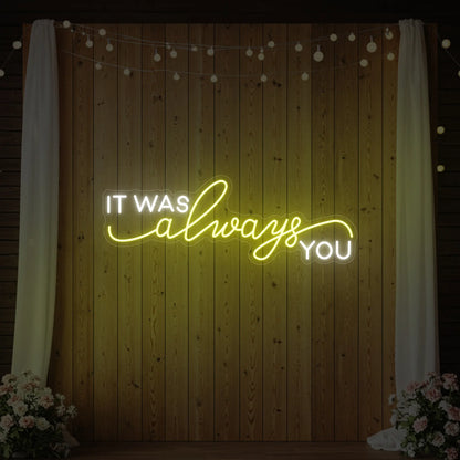 Photo of the 'It Was Always You' neon sign glowing in lemon yellow against a styled interior wall.