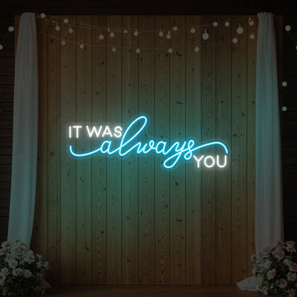 Photo of the 'It Was Always You' neon sign glowing in ice blue against a styled interior wall.