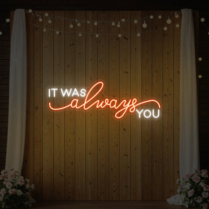 Photo of the 'It Was Always You' neon sign glowing in golden yellow against a styled interior wall.