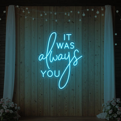 Photo of the 'It Was Always You' neon sign glowing in ice blue against a styled interior wall.