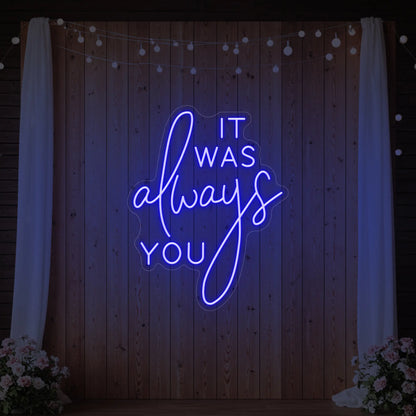 Photo of the 'It Was Always You' neon sign glowing in deep blue against a styled interior wall.