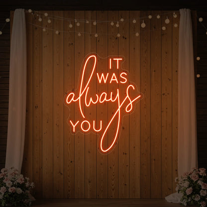 Photo of the 'It Was Always You' neon sign glowing in golden yellow against a styled interior wall.