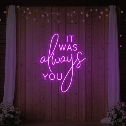 Photo of the 'It Was Always You' neon sign glowing in deep pink against a styled interior wall.
