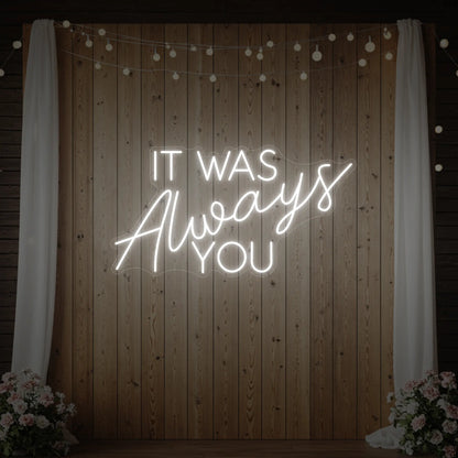 Photo of the 'It Was Always You' neon sign glowing in cool white against a styled interior wall.