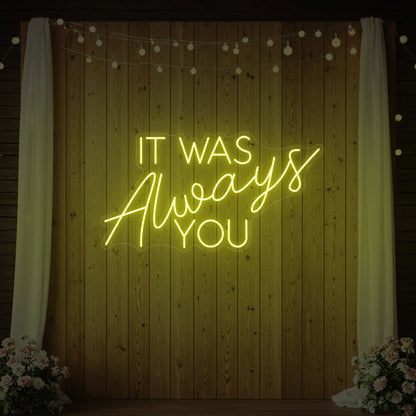 Photo of the 'It Was Always You' neon sign glowing in lemon yellow against a styled interior wall.
