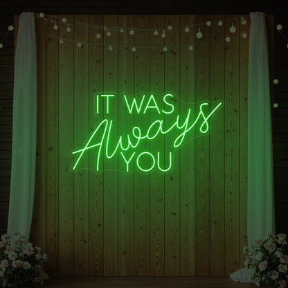 Photo of the 'It Was Always You' neon sign glowing in green against a styled interior wall.