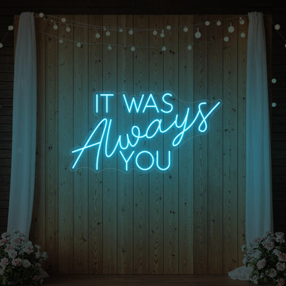 Photo of the 'It Was Always You' neon sign glowing in ice blue against a styled interior wall.