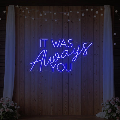 Photo of the 'It Was Always You' neon sign glowing in deep blue against a styled interior wall.