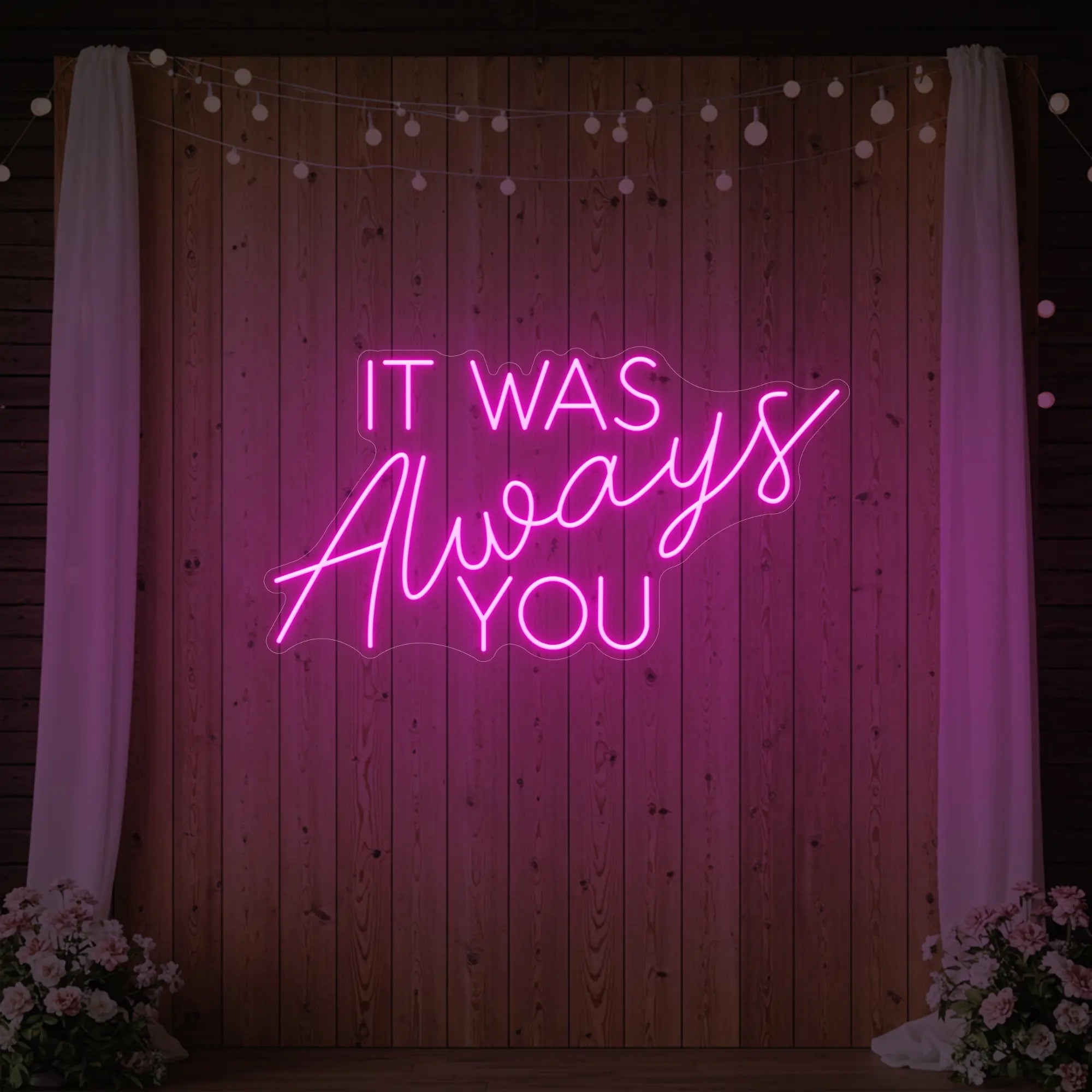 Photo of the 'It Was Always You' neon sign glowing in light pink against a styled interior wall.