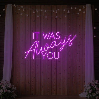 Photo of the 'It Was Always You' neon sign glowing in deep pink against a styled interior wall.