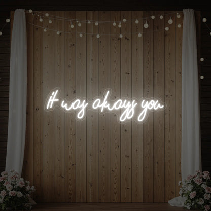 Photo of the 'It Was Always You' neon sign glowing in cool white against a styled interior wall.