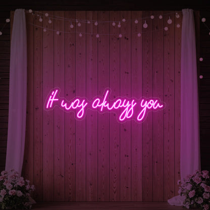 Photo of the 'It Was Always You' neon sign glowing in light pink against a styled interior wall.