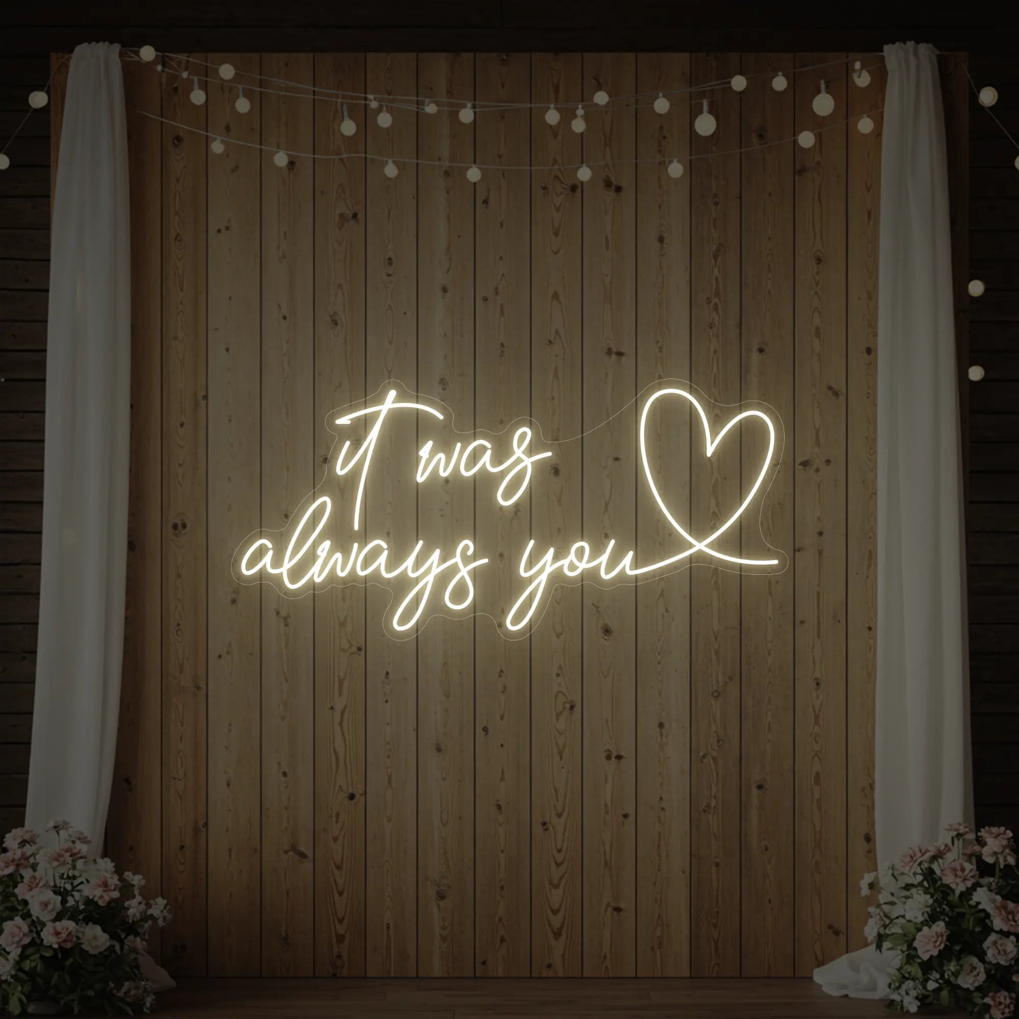 Photo of the 'It Was Always You Heart' neon sign glowing in warm white against a styled interior wall.