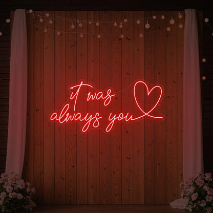 Photo of the 'It Was Always You Heart' neon sign glowing in red against a styled interior wall.