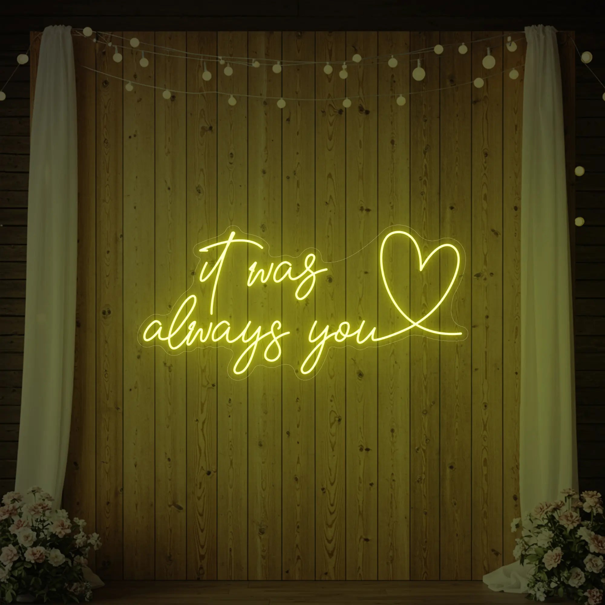 Photo of the 'It Was Always You Heart' neon sign glowing in lemon yellow against a styled interior wall.