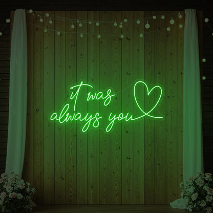 Photo of the 'It Was Always You Heart' neon sign glowing in green against a styled interior wall.