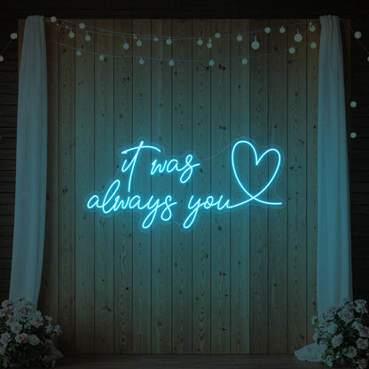 Photo of the 'It Was Always You Heart' neon sign glowing in ice blue against a styled interior wall.