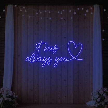 Photo of the 'It Was Always You Heart' neon sign glowing in deep blue against a styled interior wall.