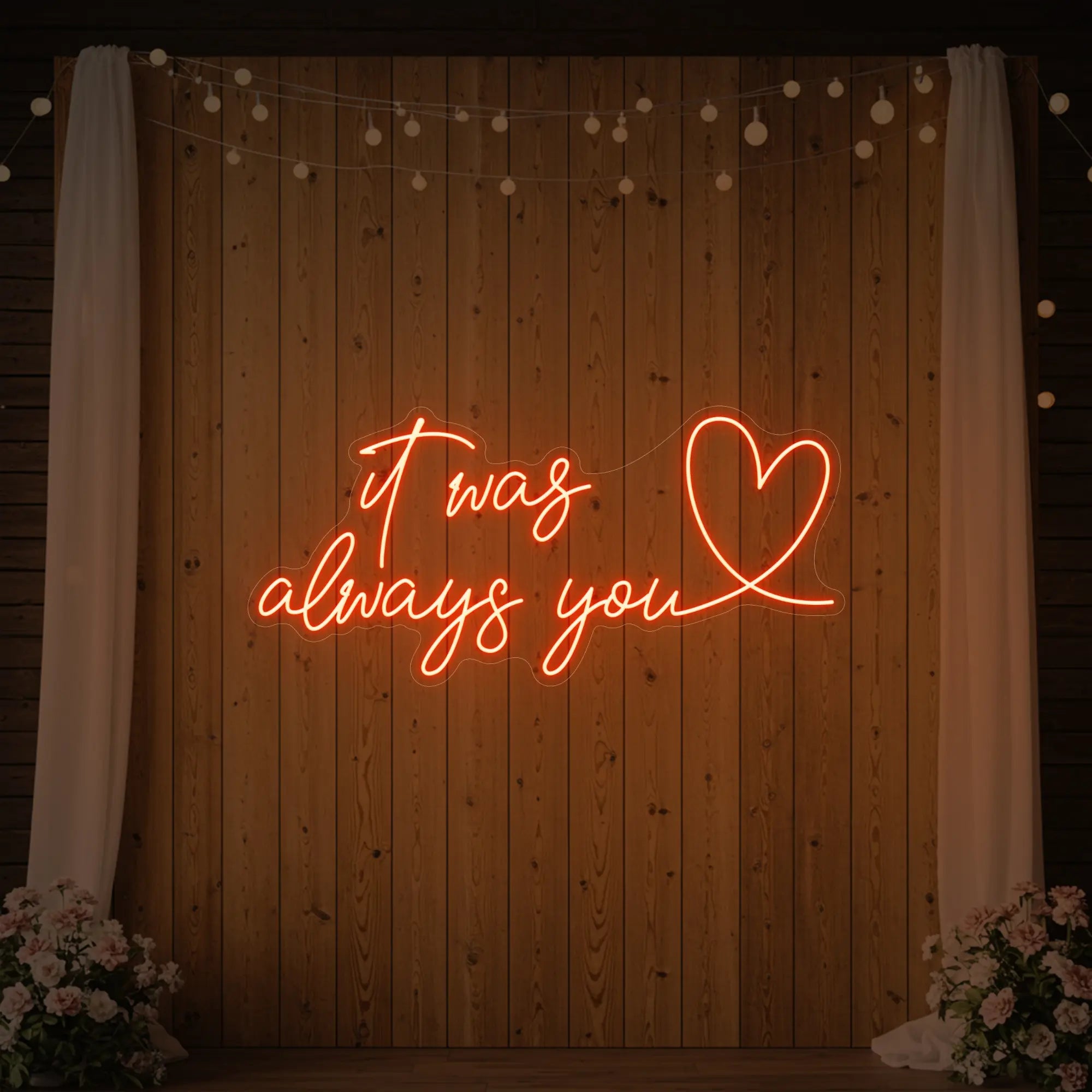 Photo of the 'It Was Always You Heart' neon sign glowing in golden yellow against a styled interior wall.