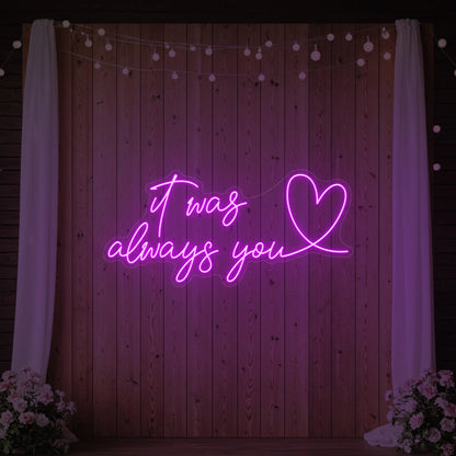 Photo of the 'It Was Always You Heart' neon sign glowing in deep pink against a styled interior wall.