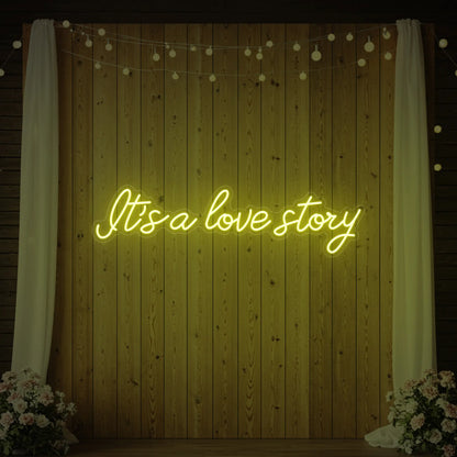 Photo of the 'It’s a Love Story' neon sign glowing in lemon yellow against a styled interior wall.