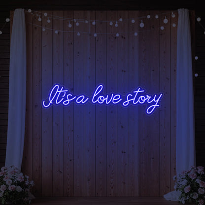 Photo of the 'It’s a Love Story' neon sign glowing in deep blue against a styled interior wall.